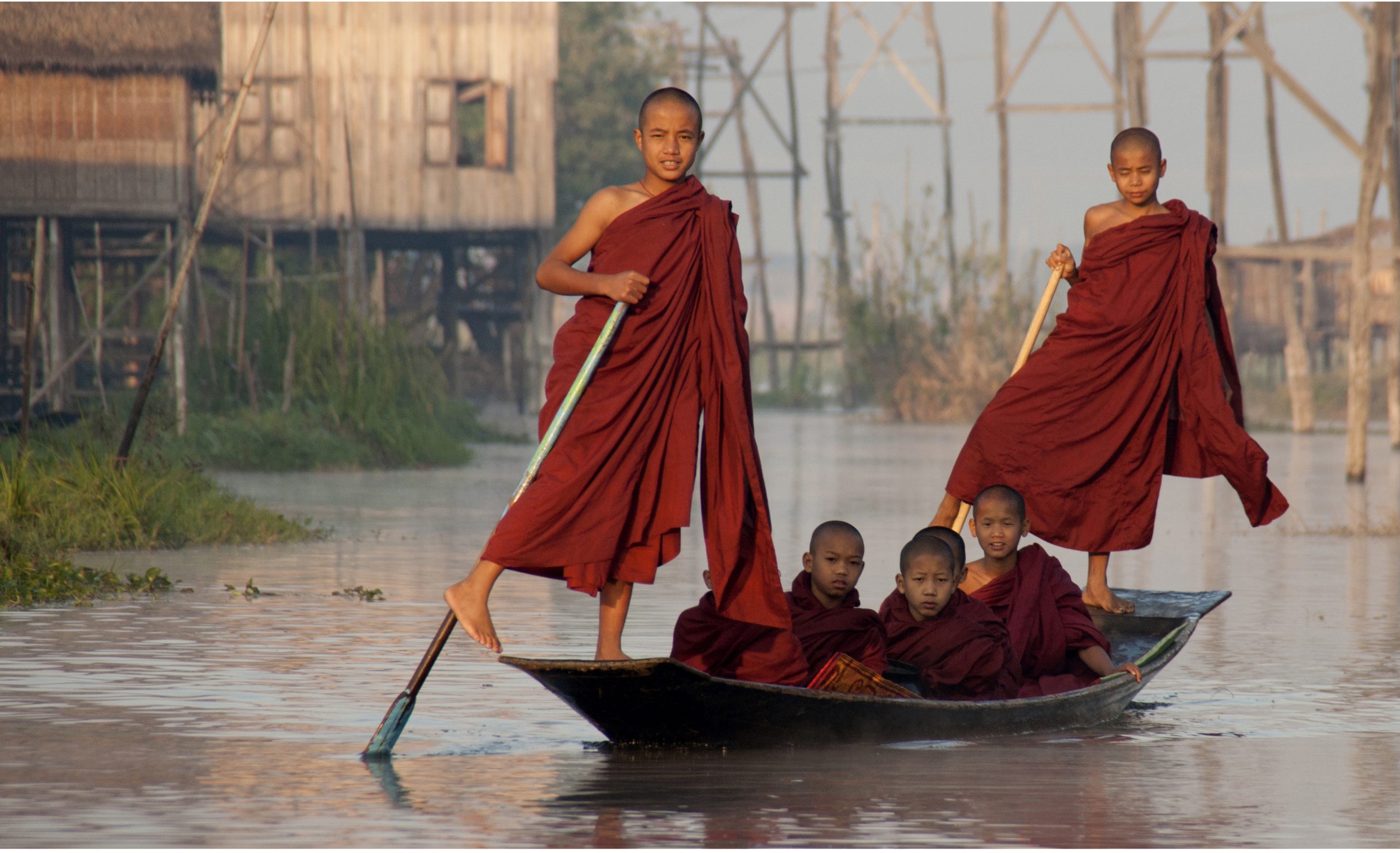 Young Buddhist monks standing on a wooden boat collecting alms on Inle Lake, Myanmar, at sunrise.