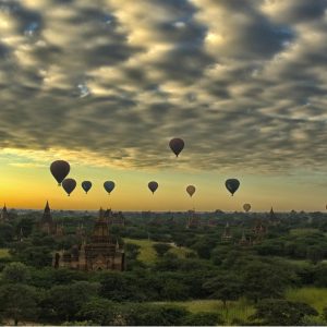 Hot air balloons floating over the temples and pagodas of Bagan at sunrise beneath a dramatic cloud-filled sky.