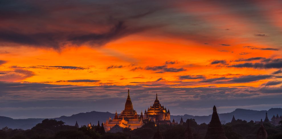 Golden temples and pagodas of Bagan silhouetted against a dramatic orange sunset sky in Myanmar.