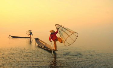 Traditional Inle Lake fishermen balancing on boats at sunrise in Myanmar cultural photography tour