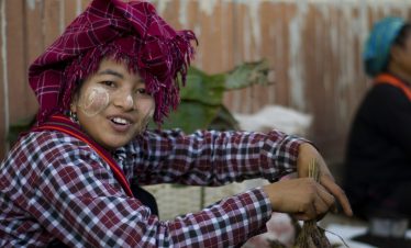 Palaung woman at a market near Inle Lake wearing a red checked headscarf and plaid shirt, with thanaka on her cheeks.