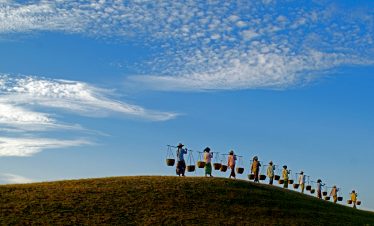 Villagers carrying baskets across a hill in rural Bagan, Myanmar.