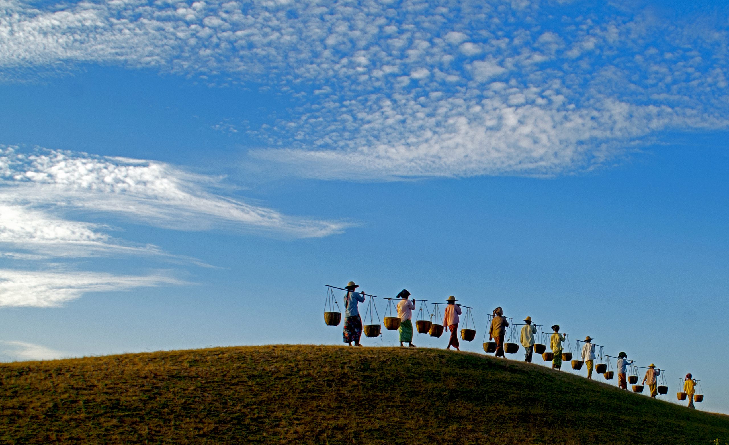 Villagers carrying baskets across a hill in rural Bagan, Myanmar.