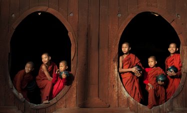 Novice monks with alms bowls framed by circular windows at Shwe Yan Pyay Monastery, Myanmar.