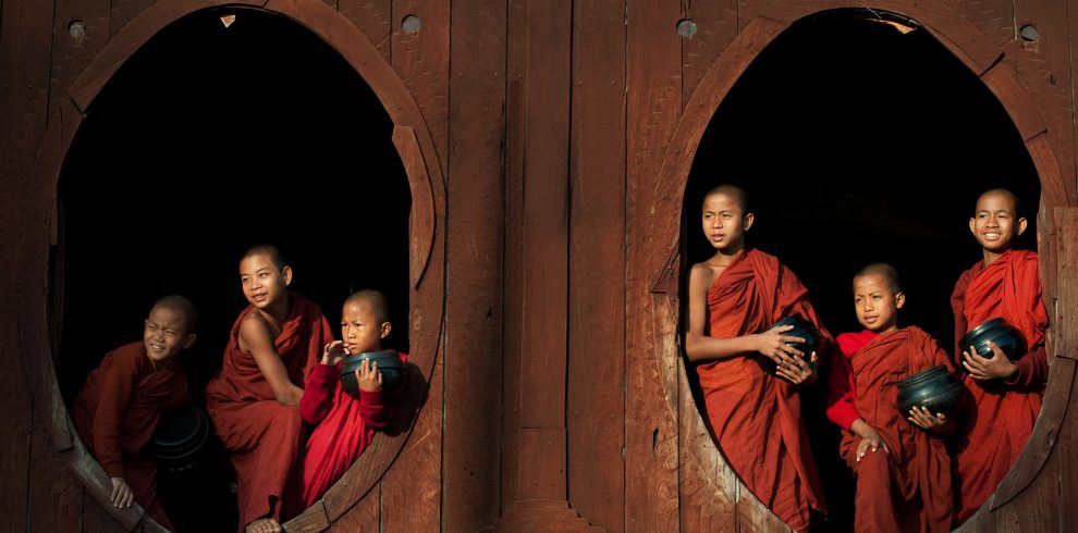 Novice monks with alms bowls framed by circular windows at Shwe Yan Pyay Monastery, Myanmar.