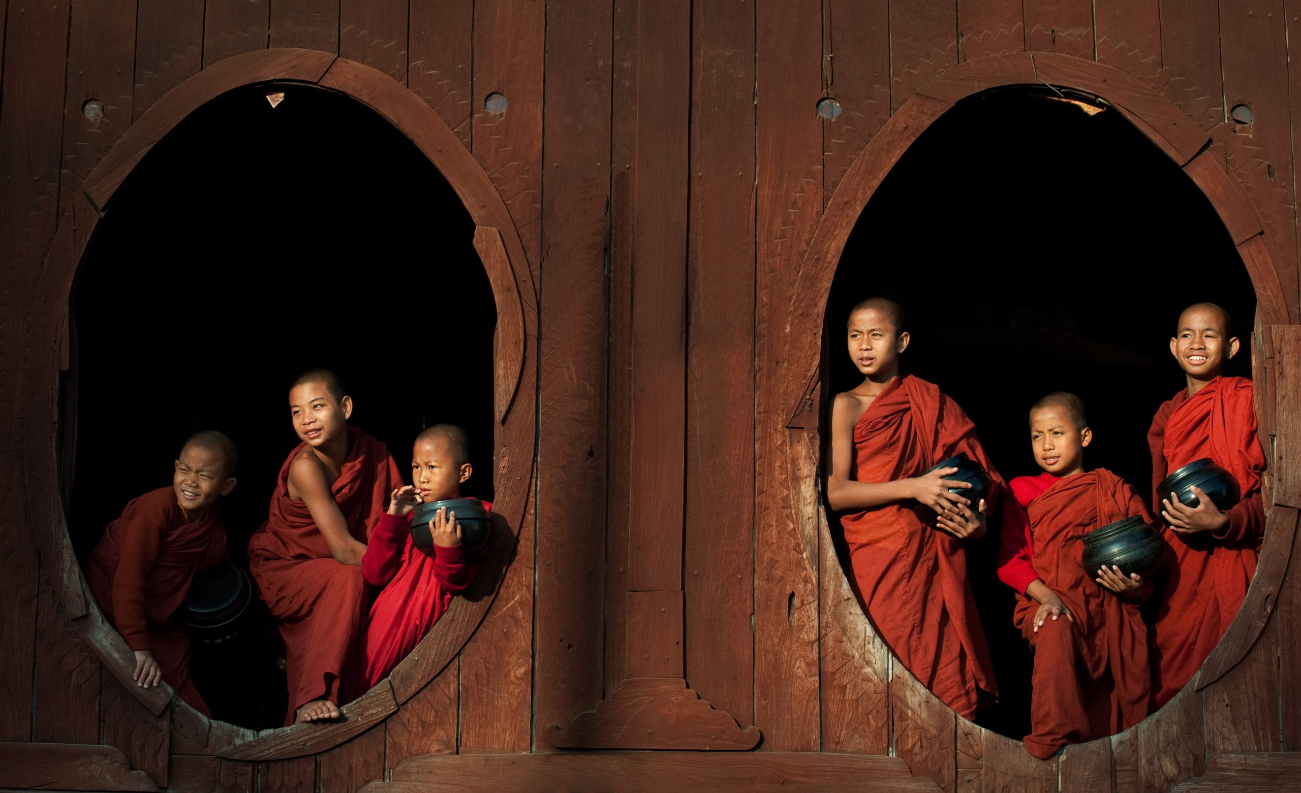 Novice monks with alms bowls framed by circular windows at Shwe Yan Pyay Monastery, Myanmar.