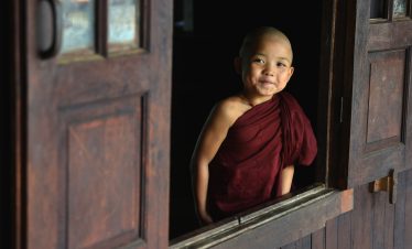 Young novice monk smiling through a wooden monastery window in Myanmar
