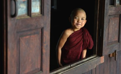 Young novice monk smiling through a wooden monastery window in Myanmar