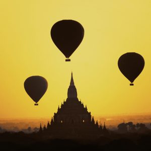 Hot air balloons floating above ancient temples of Bagan during golden sunrise in Myanmar, viewed on a Myanmar Photo Tour.
