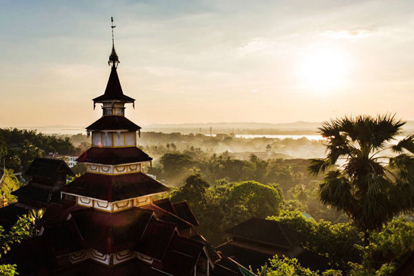 Tiered pagoda tower at sunrise above a misty treetop canopy and river valley near Mawlamyine, Myanmar.