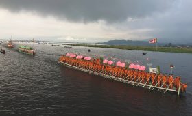 Long ceremonial boat of monks with pink umbrellas during the Phaung Daw Oo boat procession on Inle Lake under a dramatic cloudy sky.