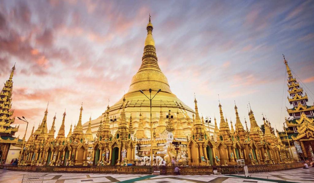 Golden Shwedagon Pagoda in Yangon at sunrise with colorful sky and detailed stupas around the main stupa.