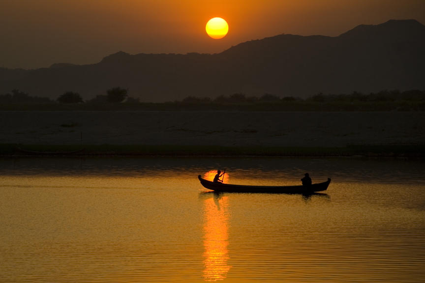 Silhouette of a fisherman paddling a long wooden boat on the river at sunset in Bagan, Myanmar.