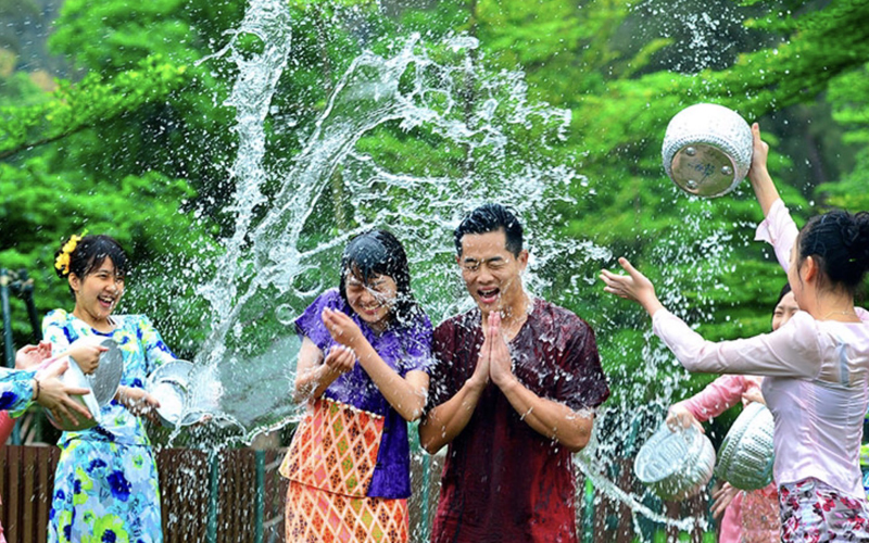 People in colorful traditional dress splashing water and laughing during the Thingyan Water Festival in Myanmar.