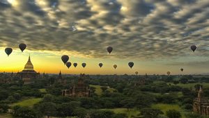 Hot air balloons floating over the temple plain of Bagan at sunrise with a dramatic cloud-filled sky.