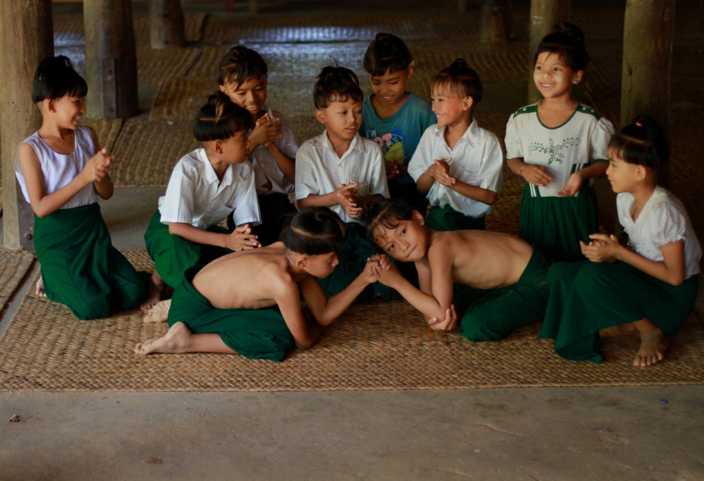 Myanmar schoolchildren playing a traditional strength game inside a rural village hall